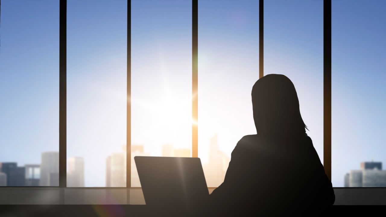 业务和人们的观念-女人剪影坐在办公室窗口背景的笔记本电脑女商人与笔记本电脑的剪影