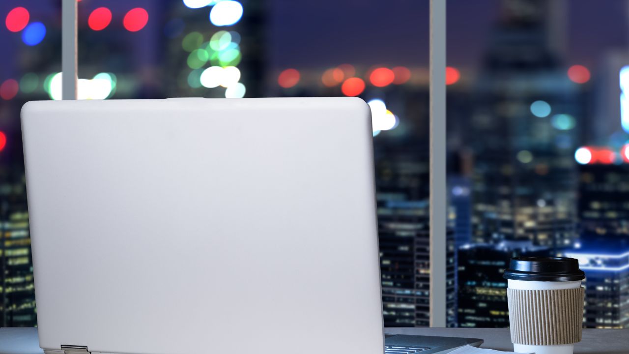 全景工作场所在桌上的膝上型计算机在办公室有商业区的现代街市摩天大楼全景夜视图